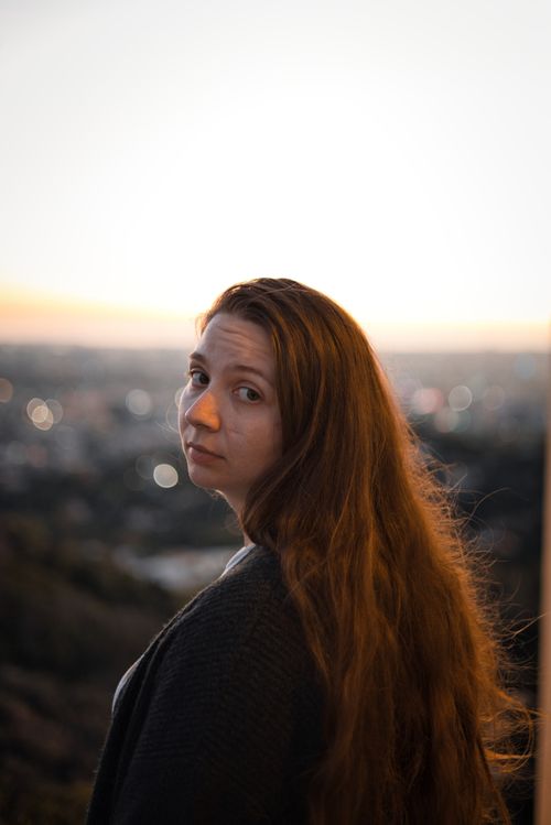 Free A woman gazes back at the camera at sunset, with a cityscape in the background. Stock Photo