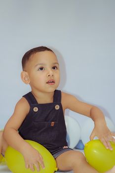 Cute child playing with colorful balloons indoors, showcasing joy and innocence.