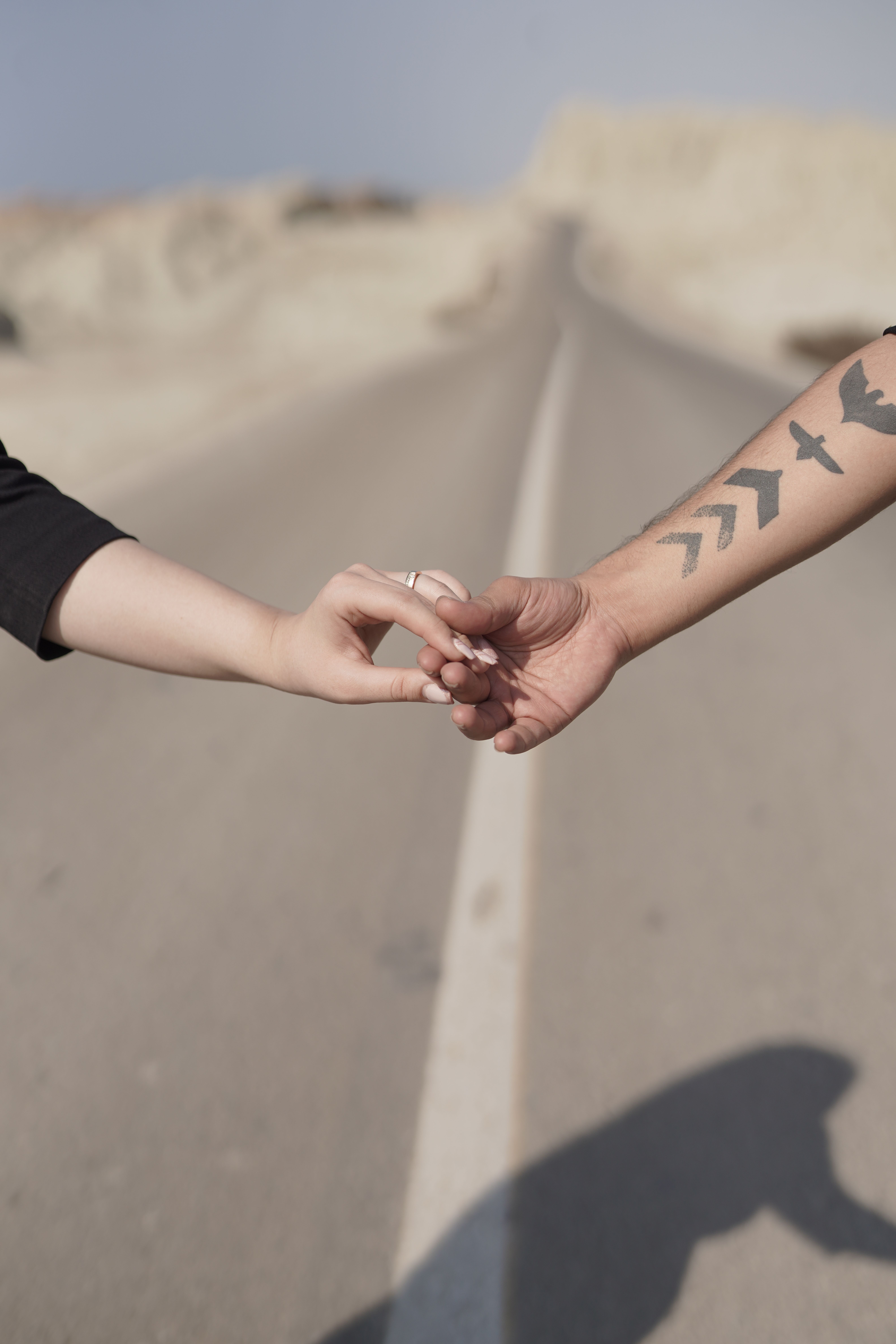A close-up of two hands reaching across an open road, symbolizing connection and journey.