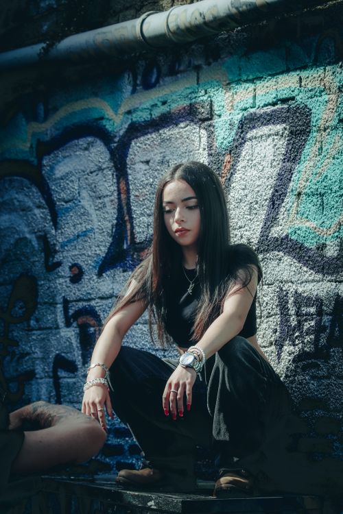 Free A young woman poses in front of a graffiti-covered wall, showcasing urban fashion style. Stock Photo