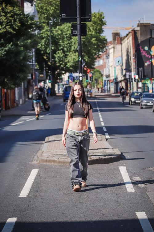 Free Confident young woman walking across a city street under bright daylight, capturing urban life. Stock Photo