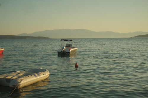 Free A serene view of motorboats floating on a calm sea during sunset with distant mountains. Stock Photo