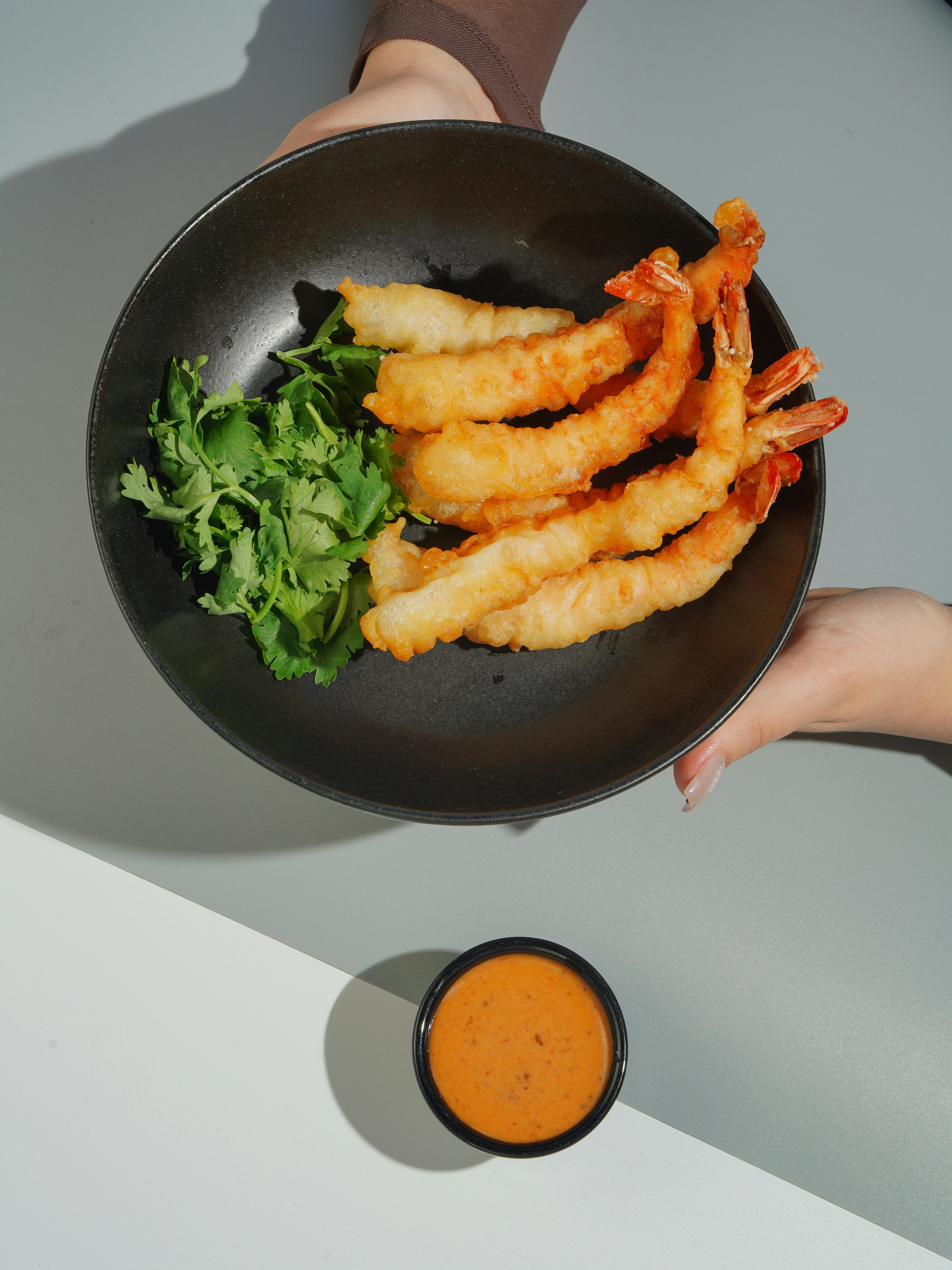 a person holding a plate with shrimp and sauce