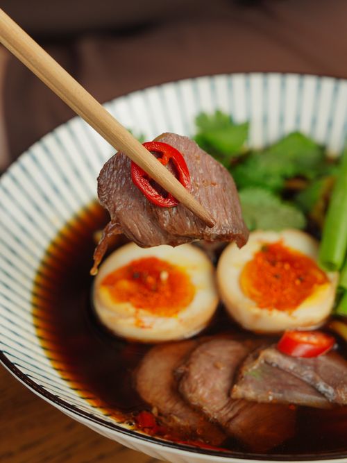 Free Close-up of flavorful beef noodle soup with boiled egg and fresh herbs. Stock Photo