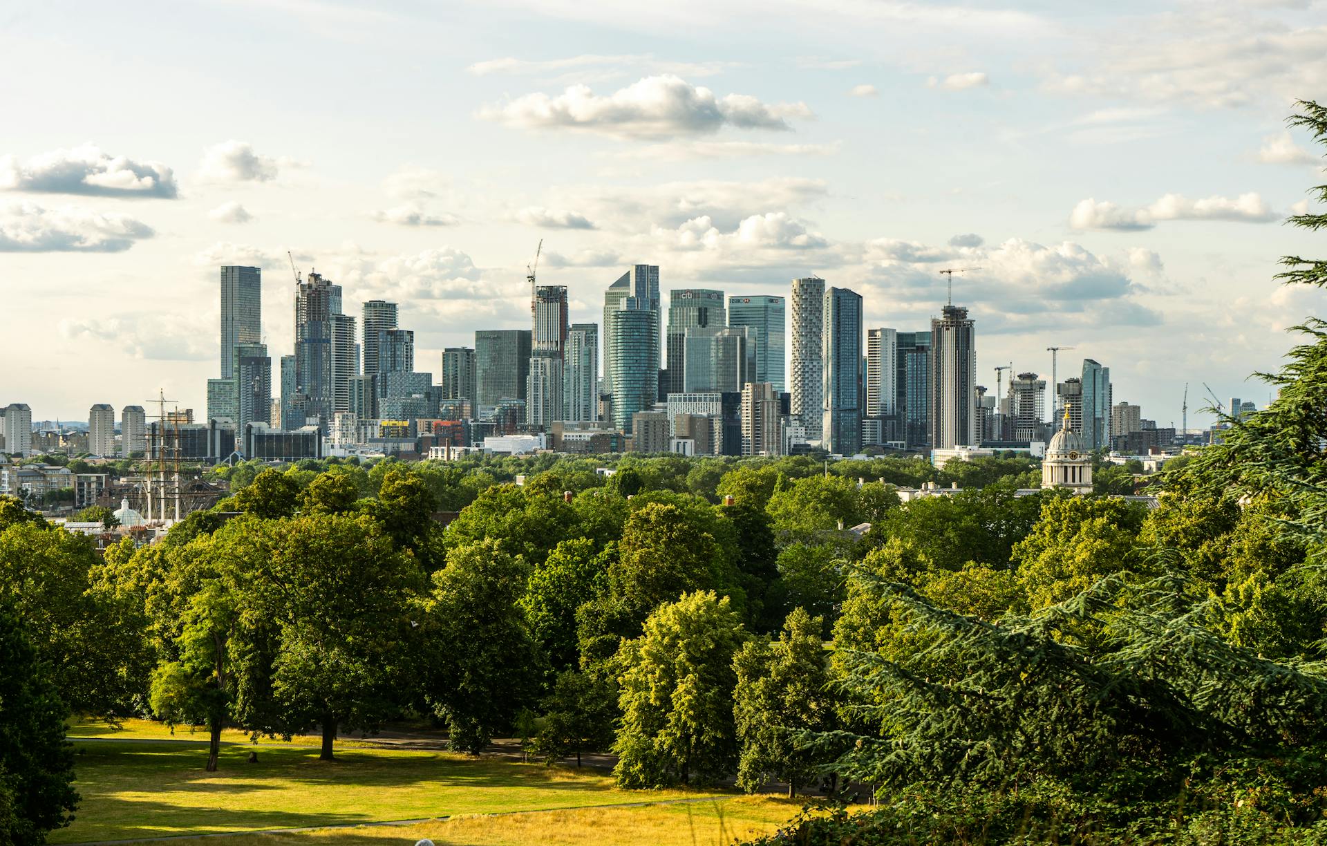 Panoramic view of London's Canary Wharf skyline from lush Greenwich Park.