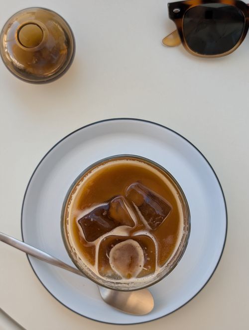 Free A refreshing iced coffee with cream, ice cubes, and vintage sunglasses on a minimalist table. Stock Photo