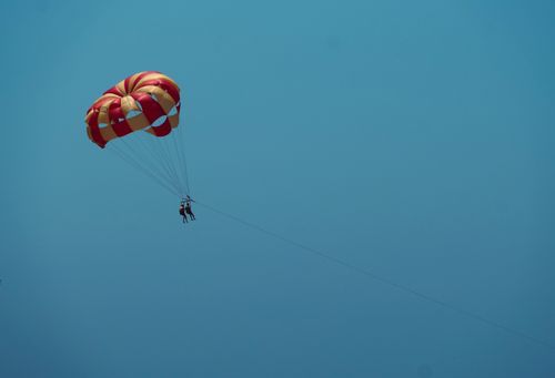 Free Thrilling parasailing adventure showcasing two people soaring high in a vibrant parachute against a clear blue sky. Stock Photo