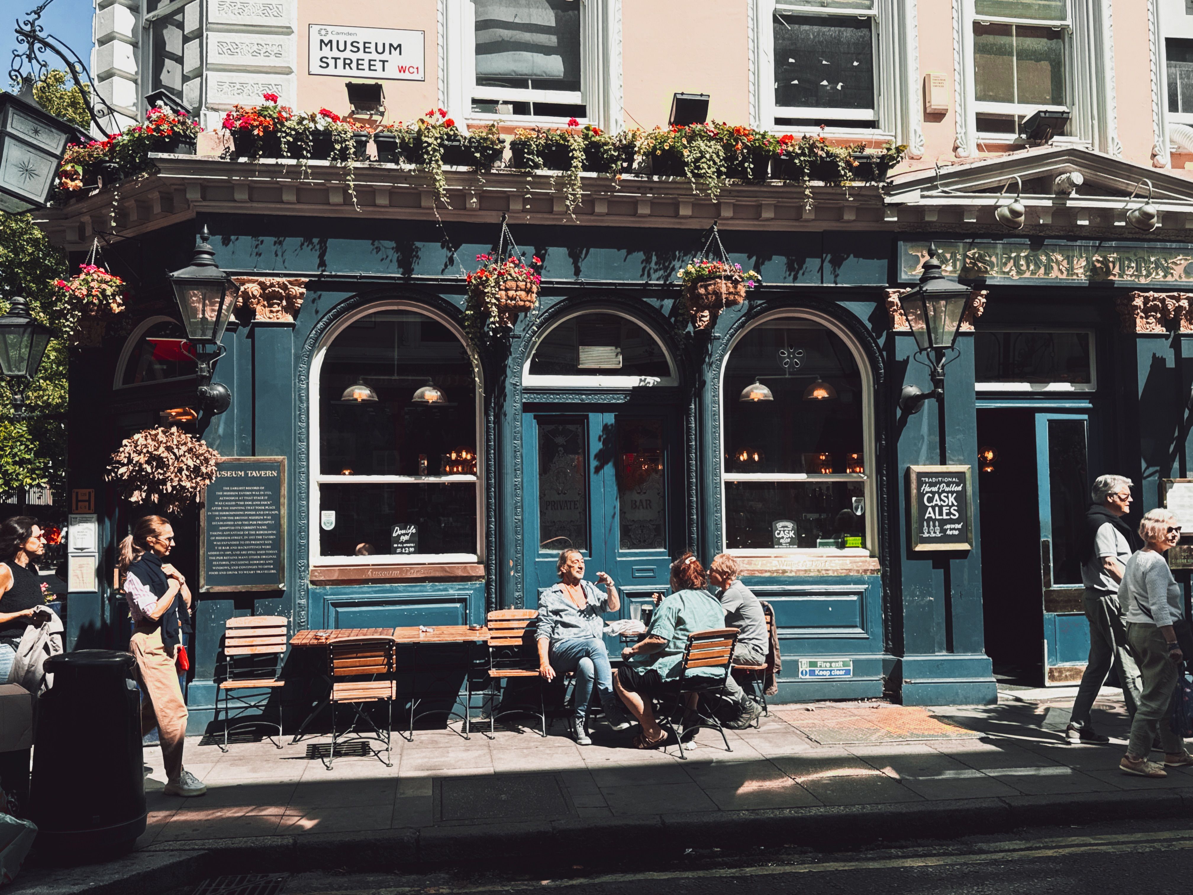 People enjoying a sunny day outside a historical pub on Museum Street, London.