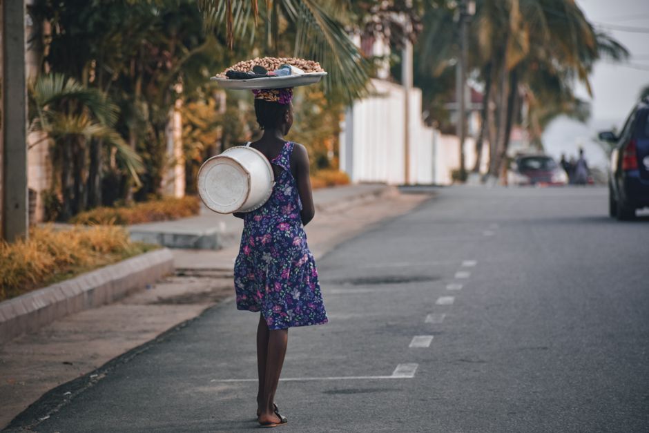 A woman walks down a Monrovian street carrying goods on her head in a vibrant dress.