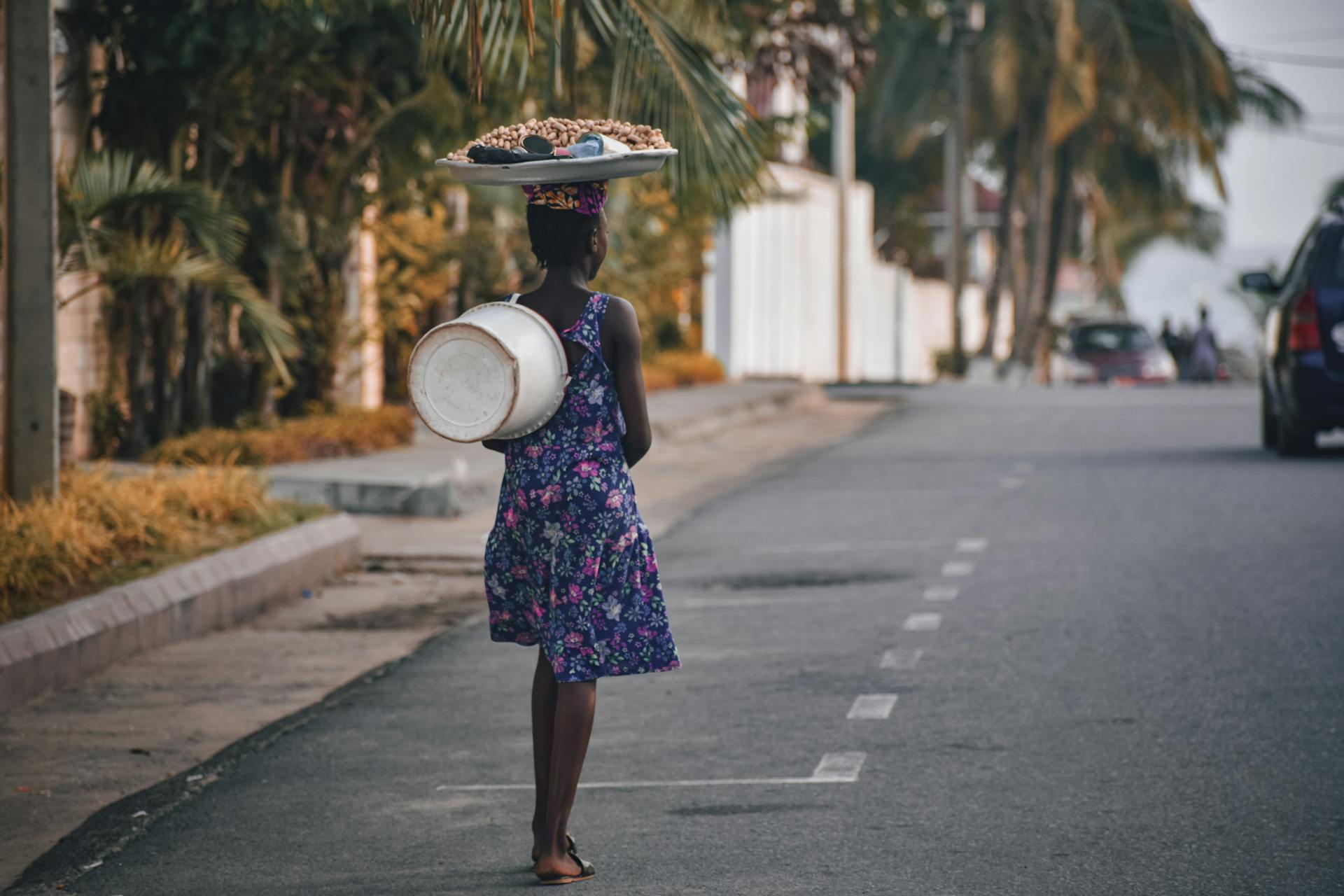 A woman walks down a Monrovian street carrying goods on her head in a vibrant dress.