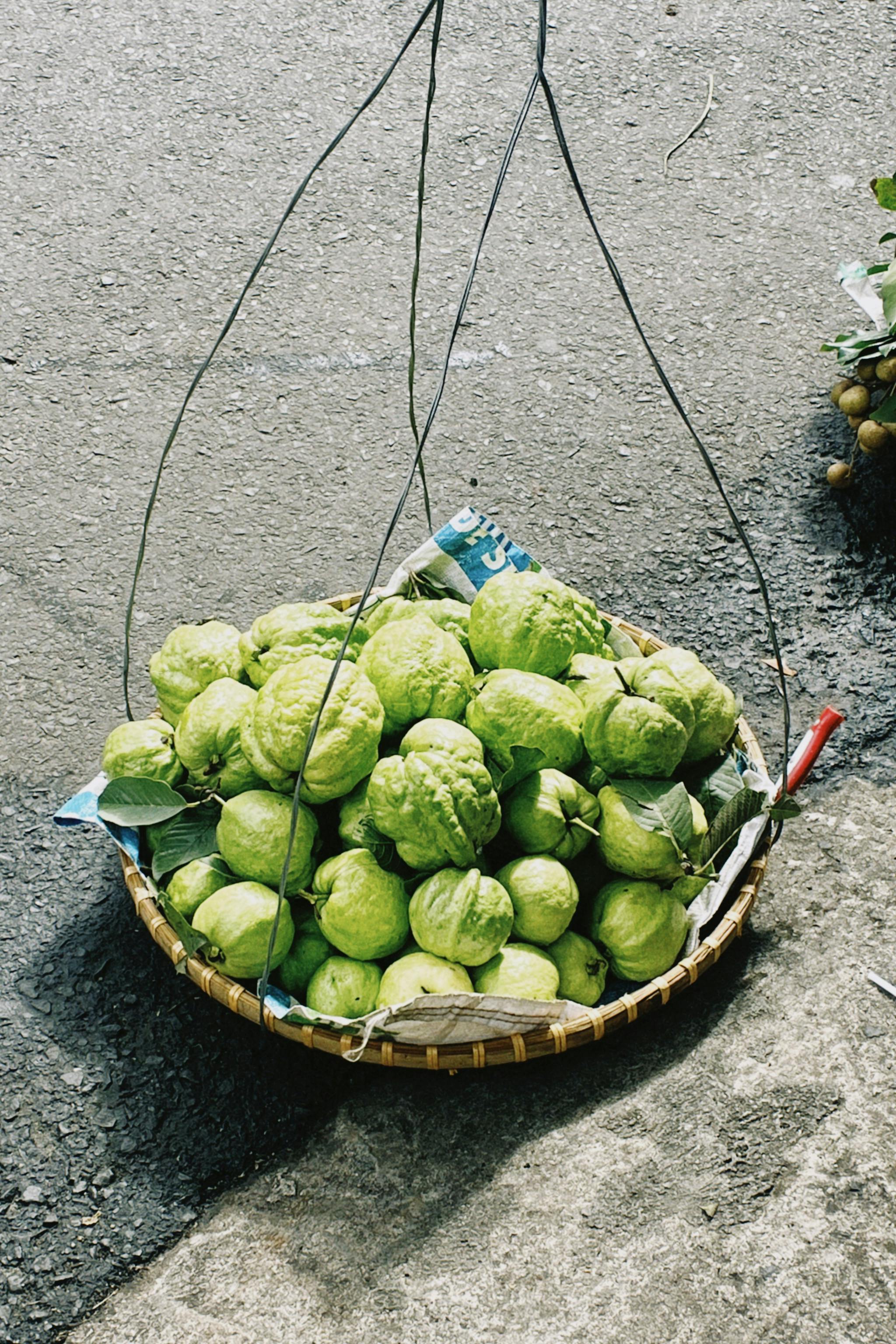 A basket of fresh green guavas displayed outdoors, showcasing natural street market vibes.
