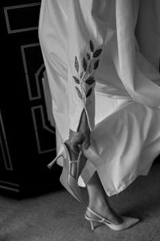 Chic black and white image of a woman in a stylish outfit, adjusting her heel.