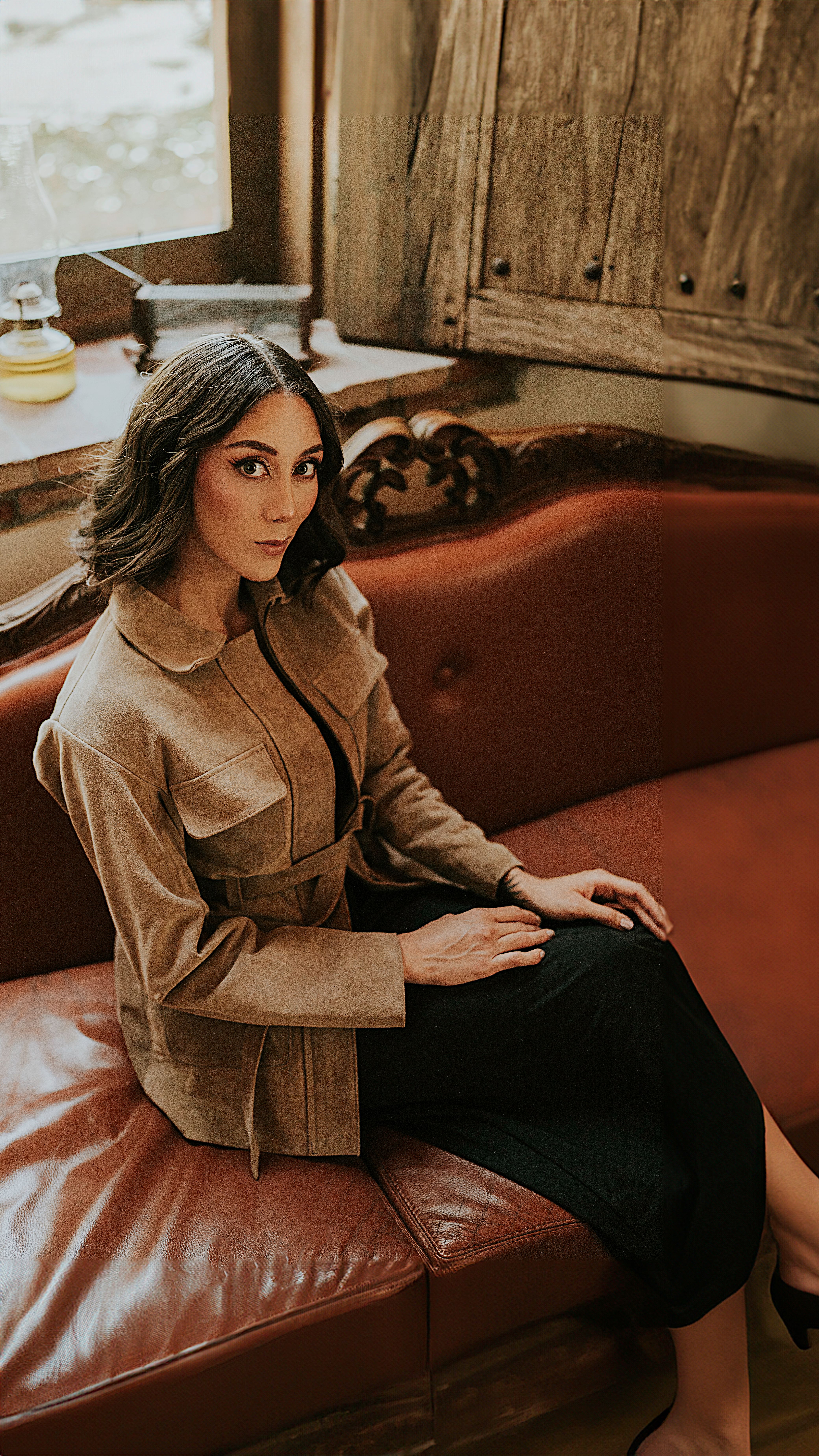 A woman in a black dress and brown jacket sitting on a red couch · Free ...