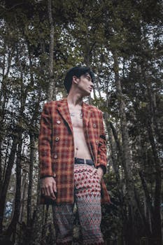 一位时尚的亚洲男子穿着有图案的夹克和裤子，在森林里摆姿势