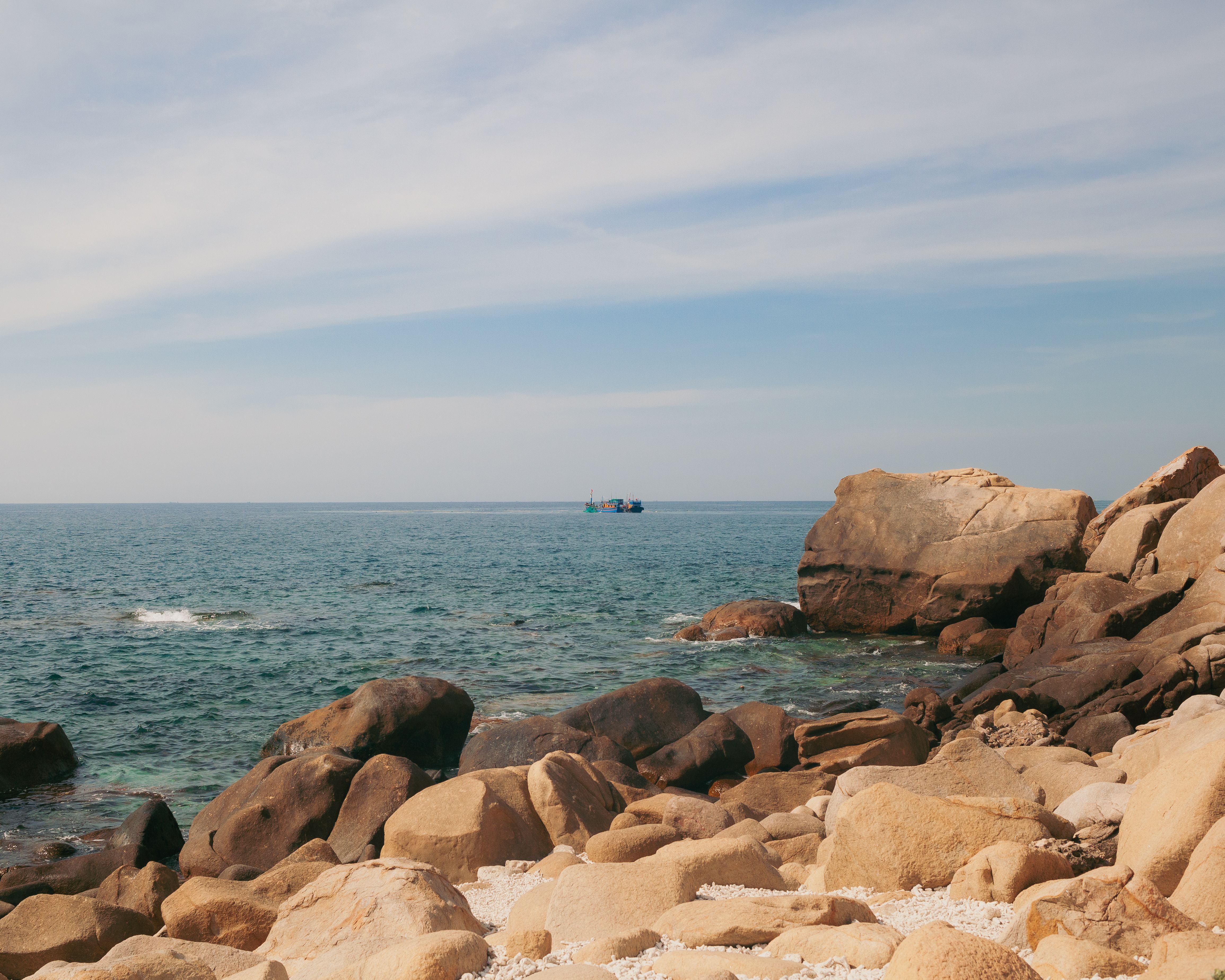 Beautiful rocky coastline in Phan Rang, Vietnam with a serene view of the ocean and distant boat.