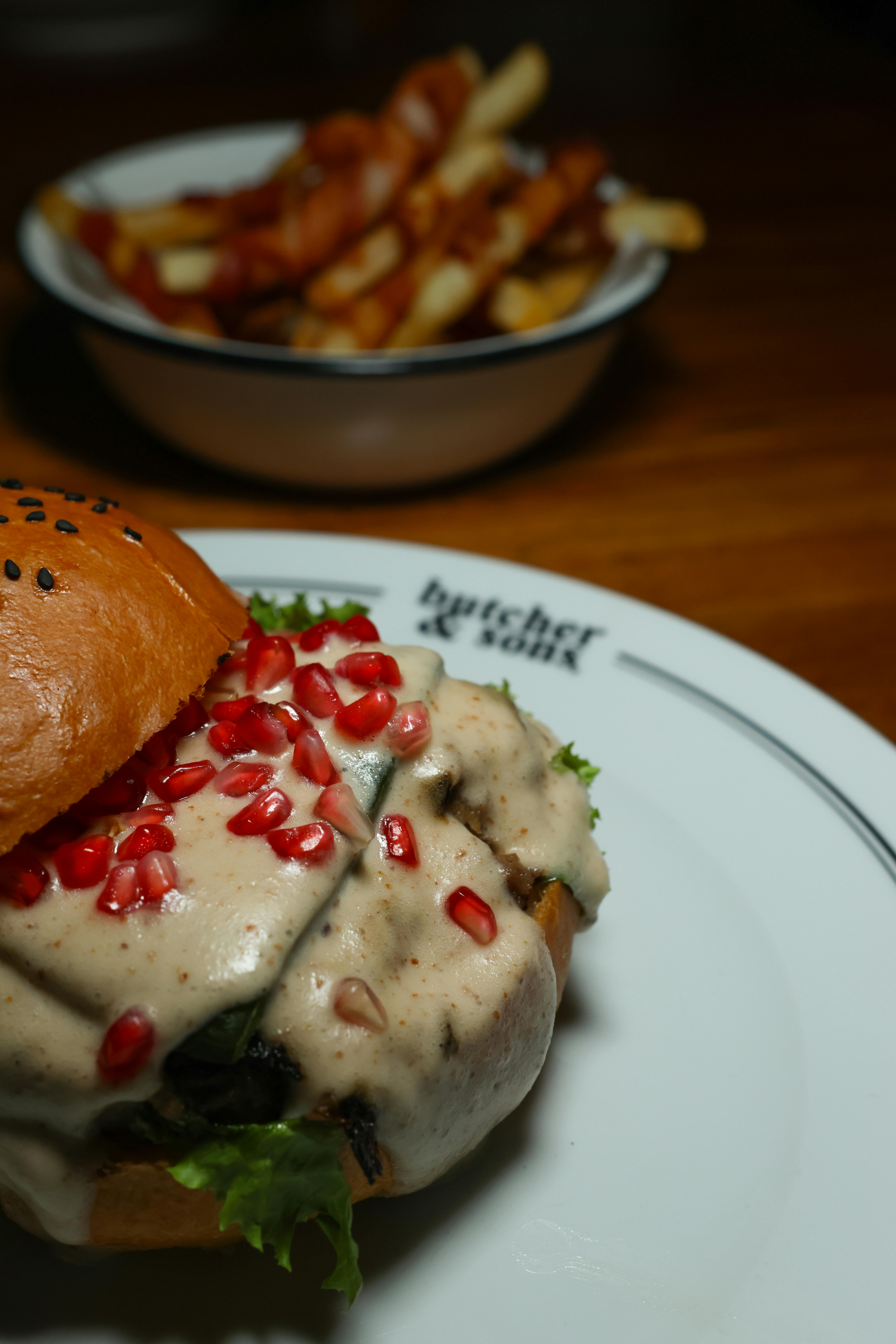 a burger with pomegranate sauce and fries on a plate