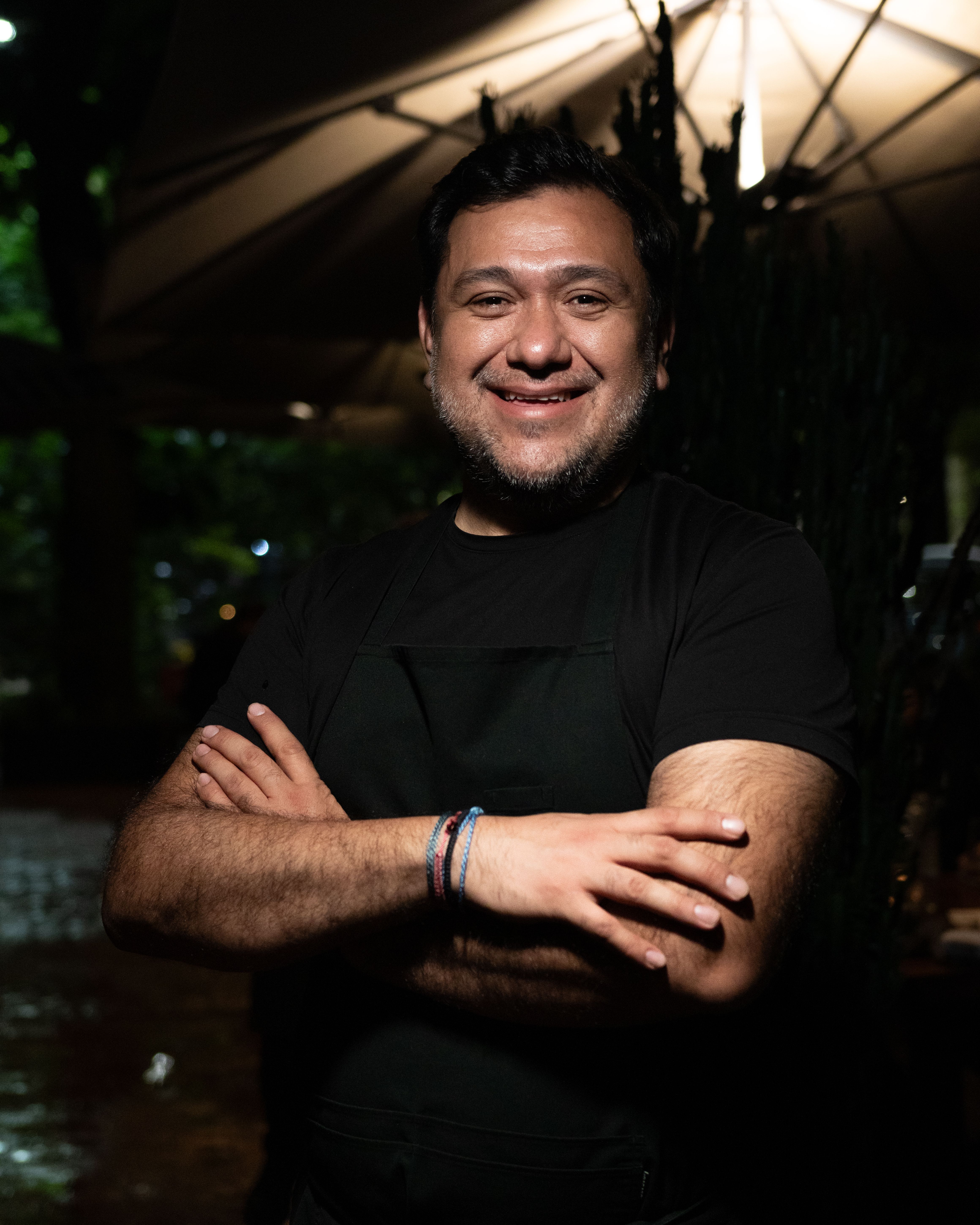 Portrait of a smiling chef standing outdoors at night, showcasing hospitality with a welcoming smile.
