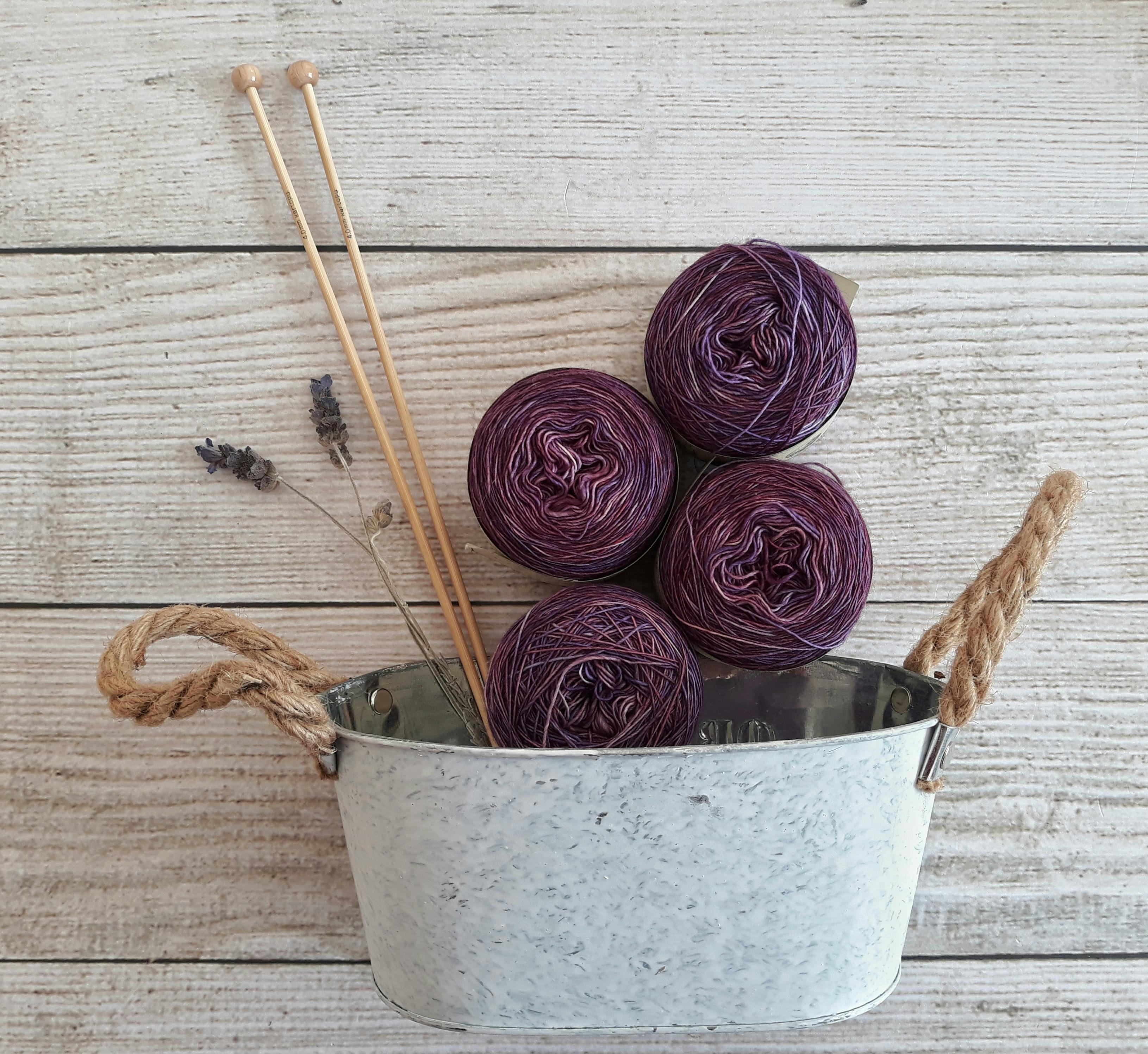 A captivating still life of purple yarn balls with knitting needles in a rustic container.