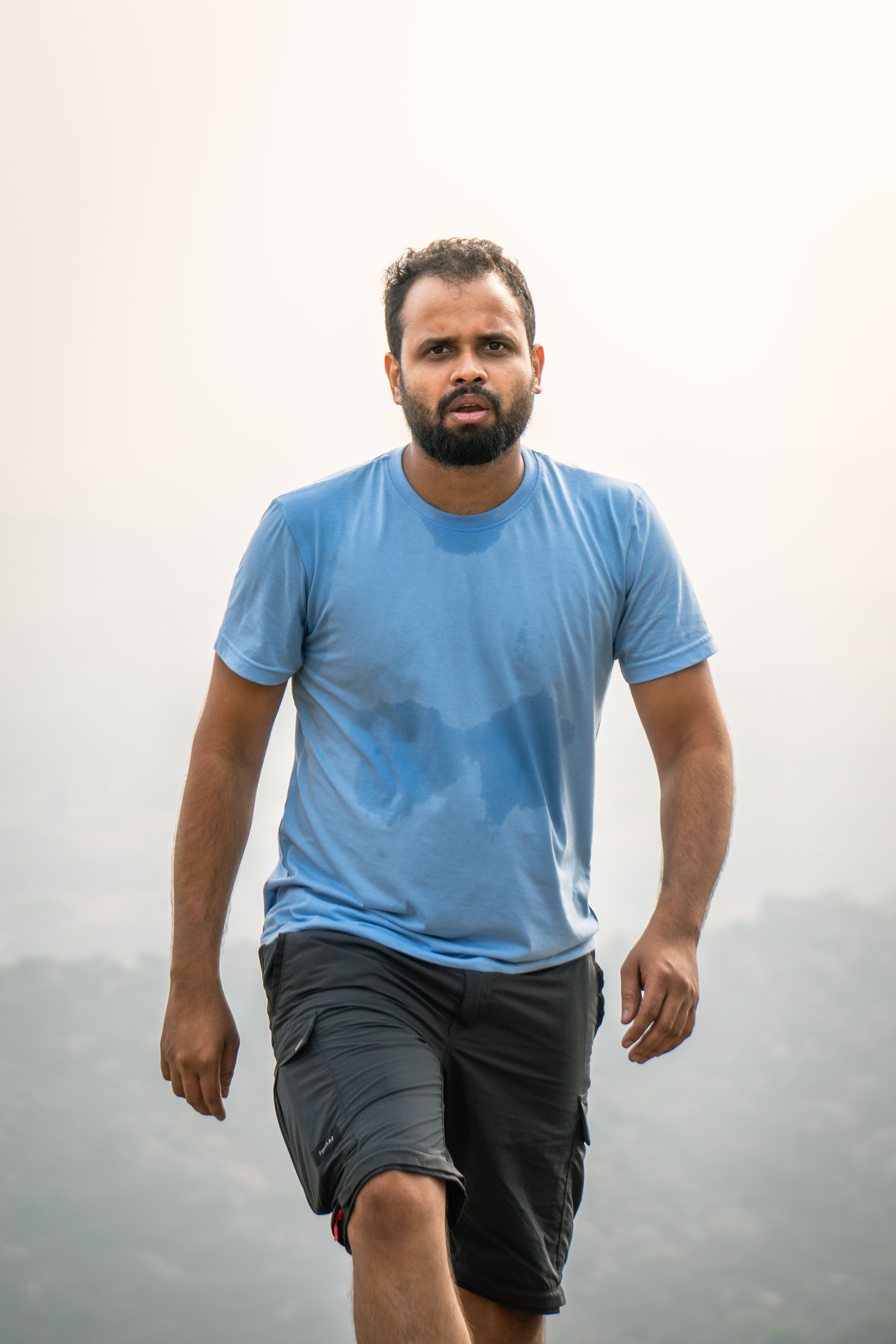 A fit young man with a beard walking outdoors on a summer day, showcasing casual and energetic style.
