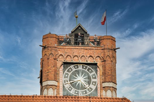 Close-up of a brick clock tower with Roman numerals in Gdansk, Poland, featuring a Polish flag.