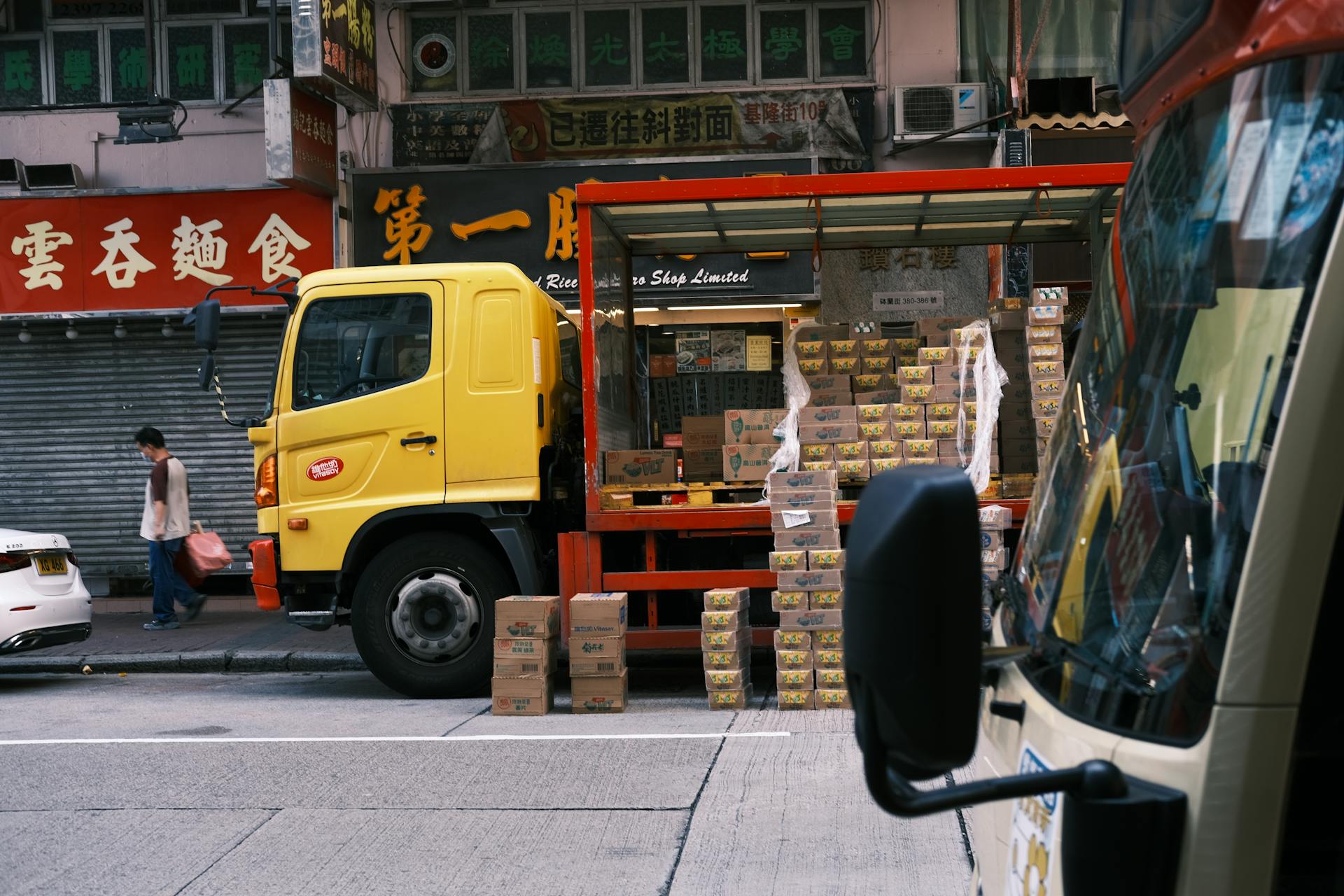 A yellow delivery truck unloading boxes in a bustling urban street market.