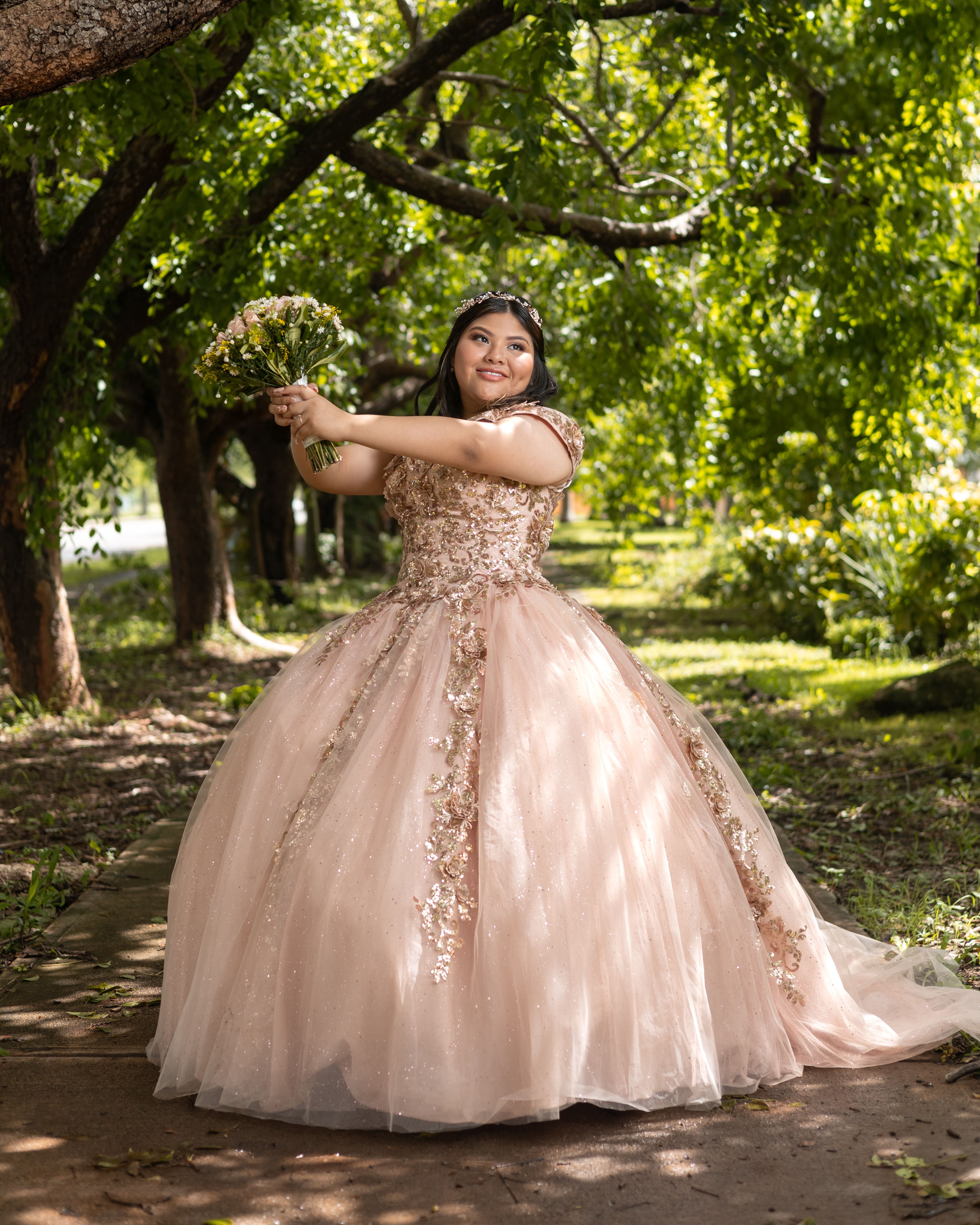 Beautiful quinceañera in a pink gown holding a bouquet in Mérida, Mexico park.