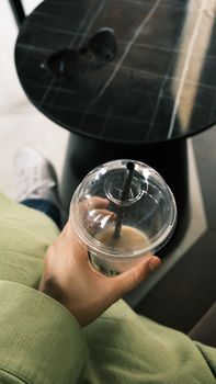 Overhead view of a person holding a coffee cup near a round table with sunglasses.