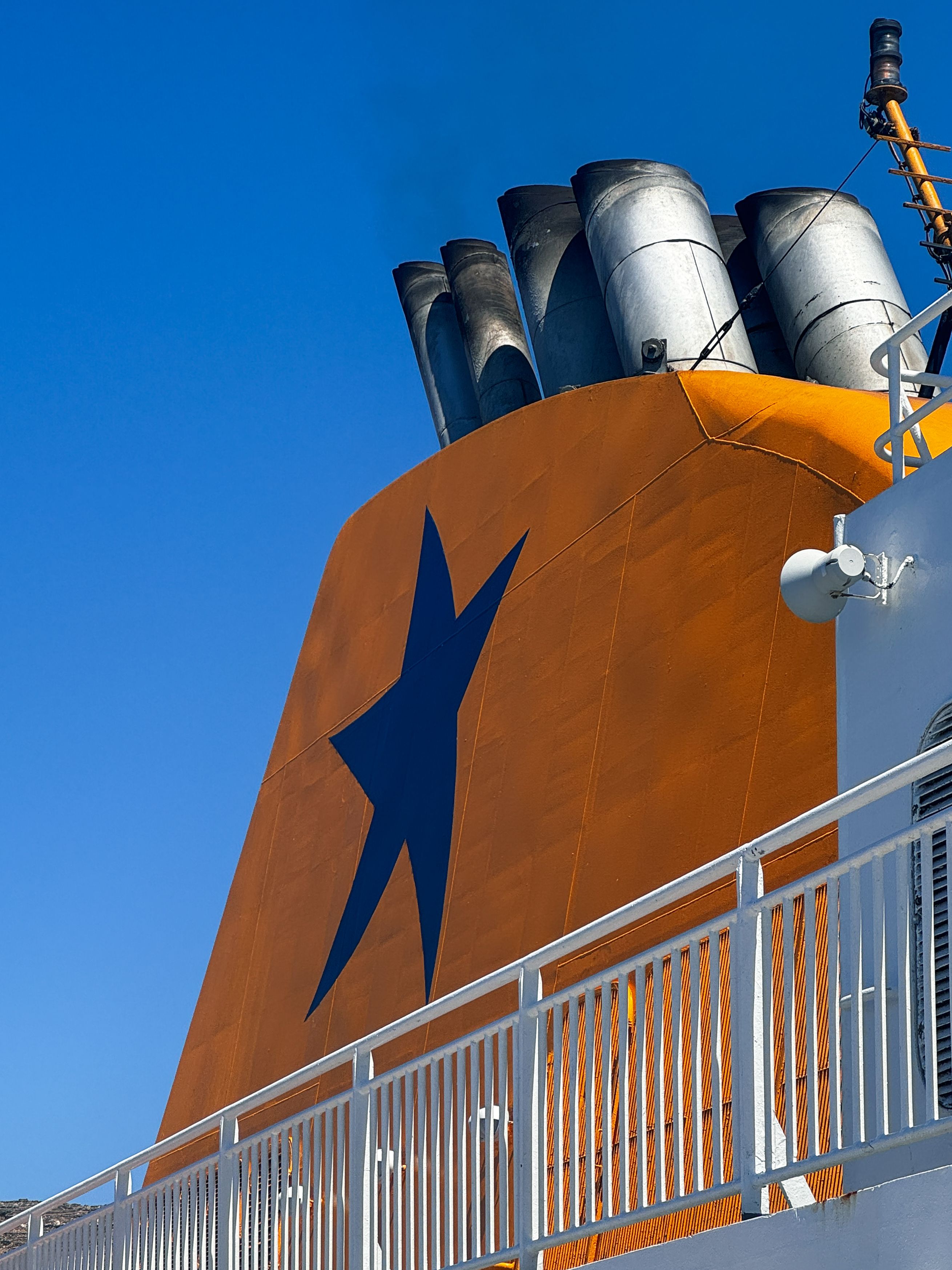Close-up of a ferry funnel featuring a bold star design under a clear blue sky in Tinos, Greece.