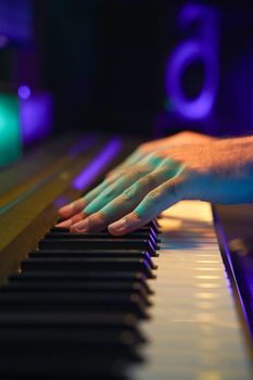 Hands playing piano keyboard under colorful studio lights, creating a jazz performance atmosphere.