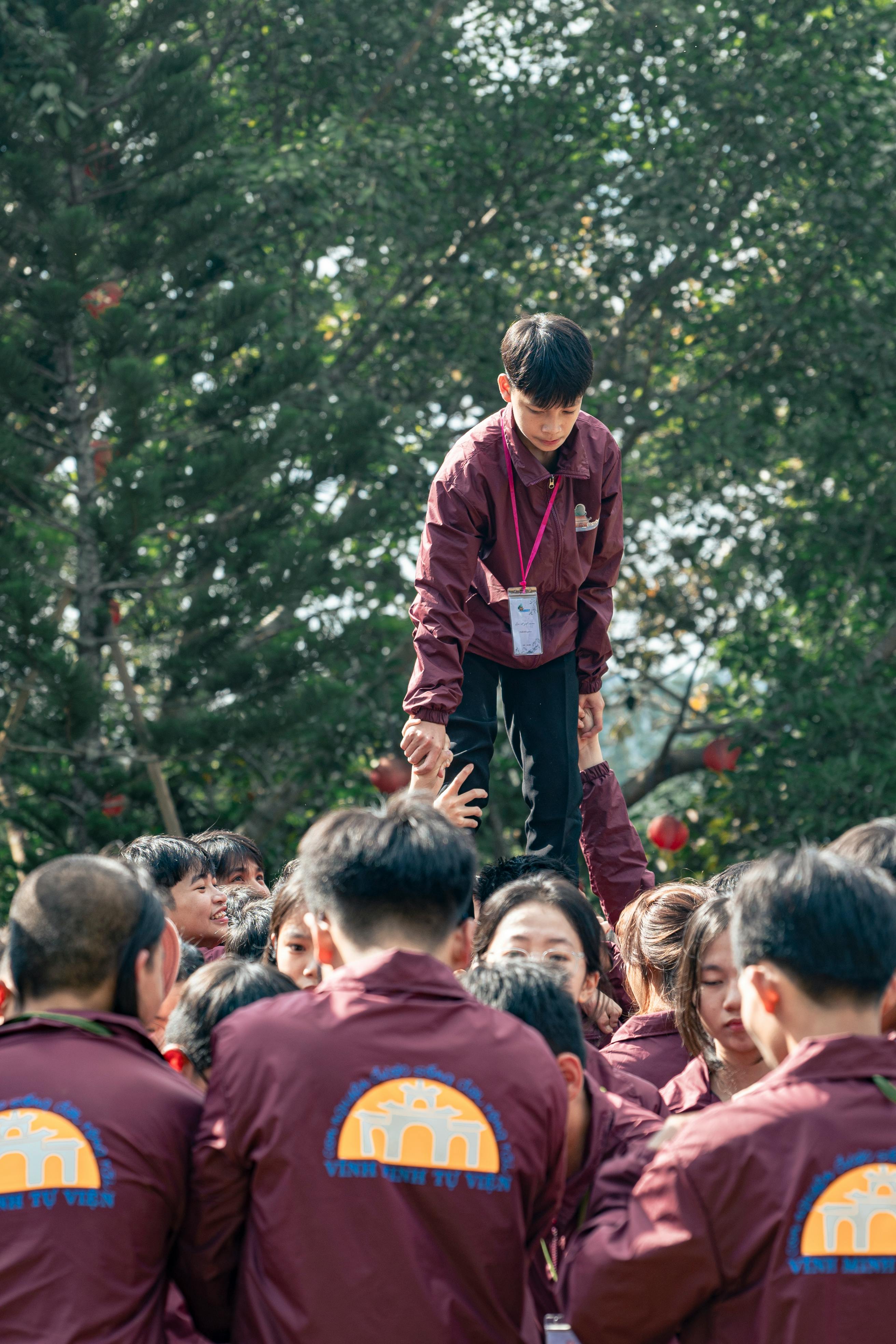 A group of people participating in a team-building activity outdoors under trees, showing teamwork and coordination.