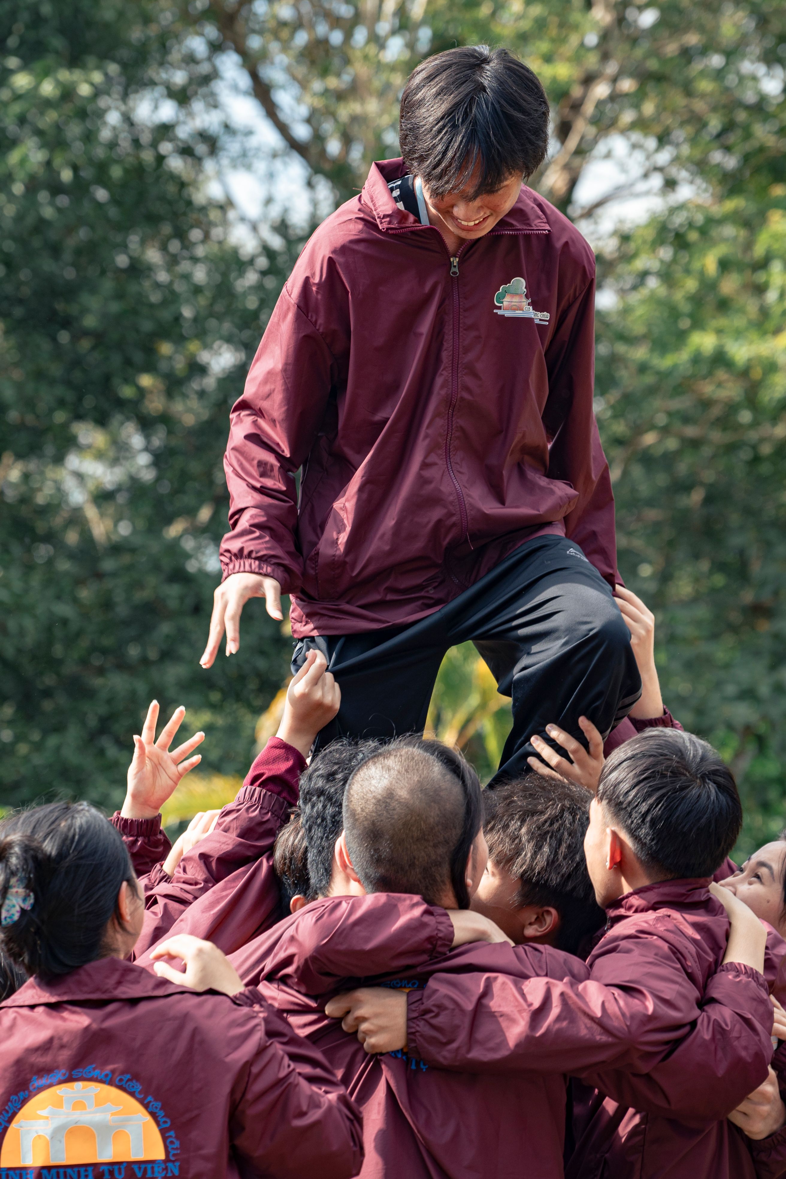 A group of children in maroon jackets are standing on top of each other ...