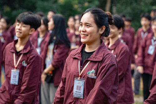 Free Group of young adults smiling outdoors, wearing maroon jackets with badges, having a lively gathering. Stock Photo