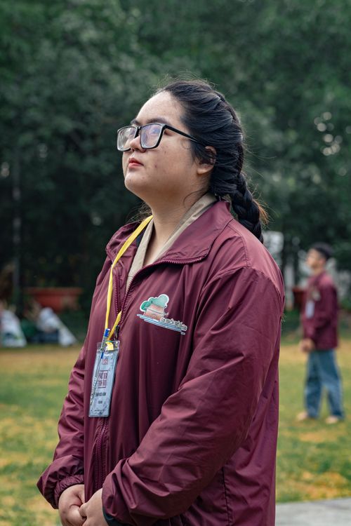 Free Young woman outdoors in a park, looking thoughtful, wearing glasses and a maroon jacket. Stock Photo