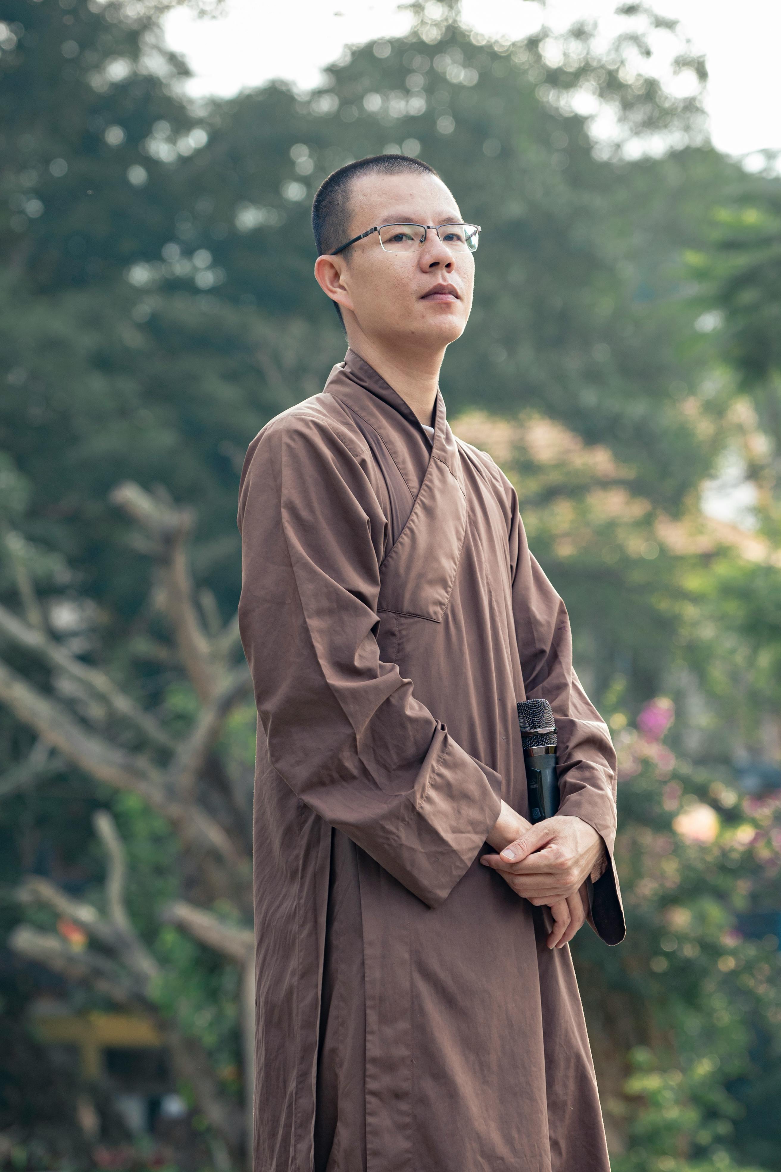 A calm monk in traditional attire enjoys a tranquil outdoors with a serene background.