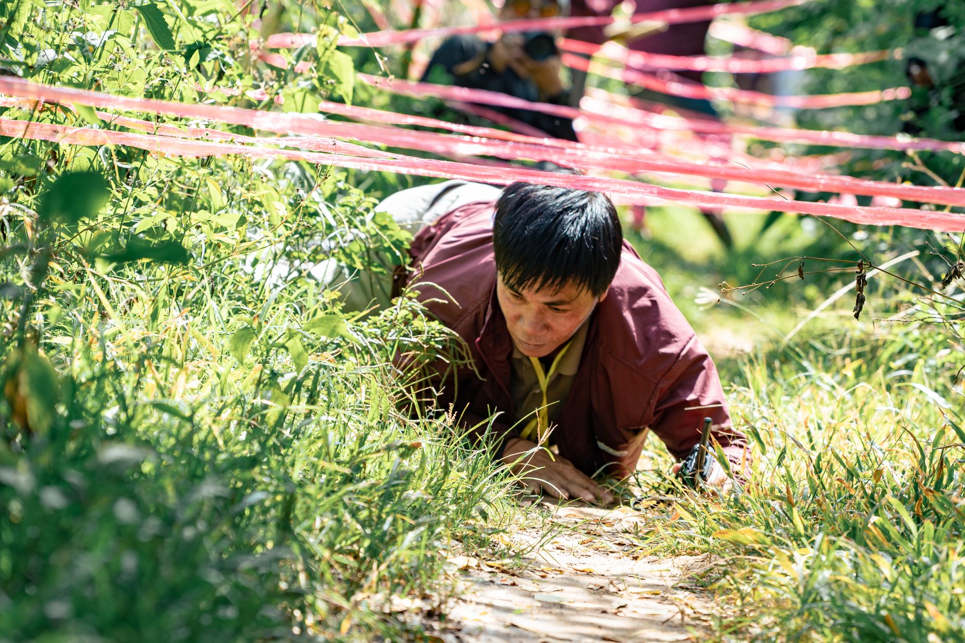 A man crawls under ropes in an outdoor obstacle course challenge.
