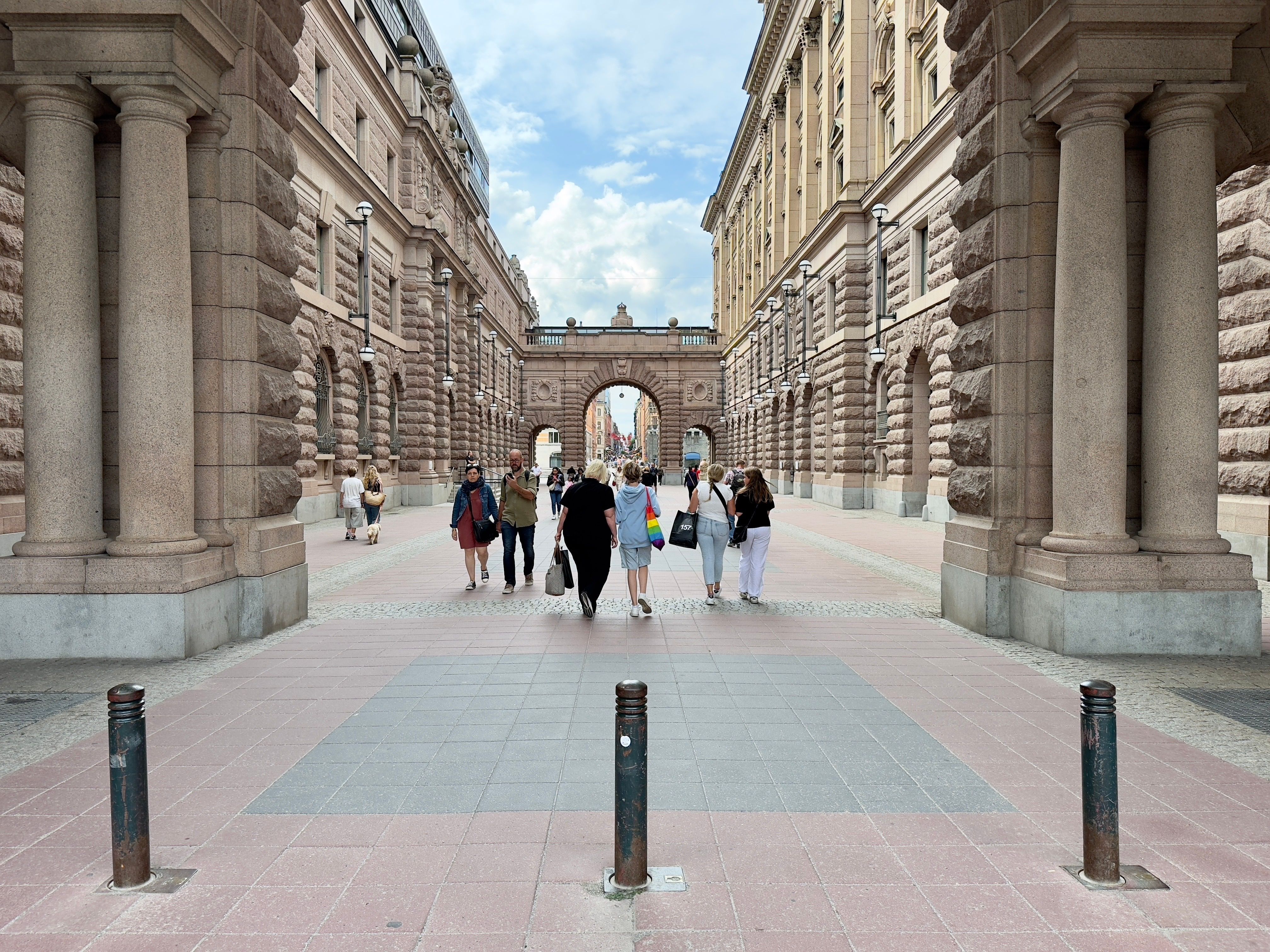 People walking through historic stone arches in central Stockholm, summer day.