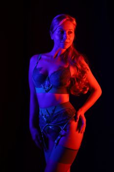 Elegant lingerie model posed under vibrant blue and red lighting, exuding glamour and style.