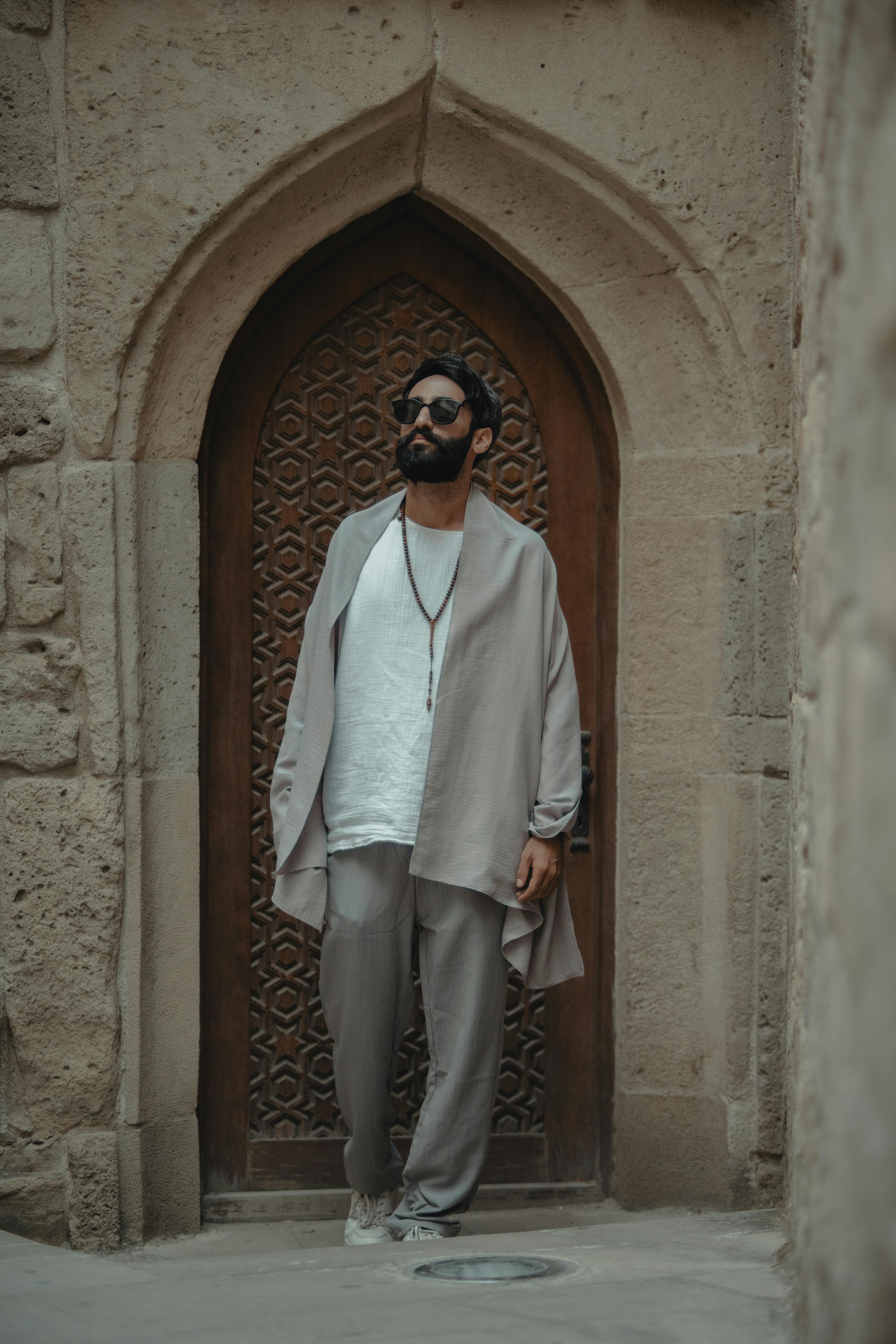 A man in a grey coat and white pants standing in front of a doorway