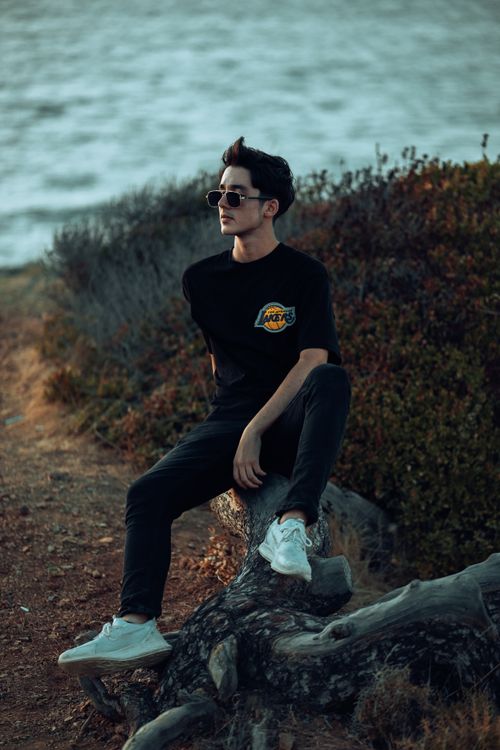 Free Fashionable young man sitting on a log by the lake during sunset, exuding a relaxed vibe. Stock Photo