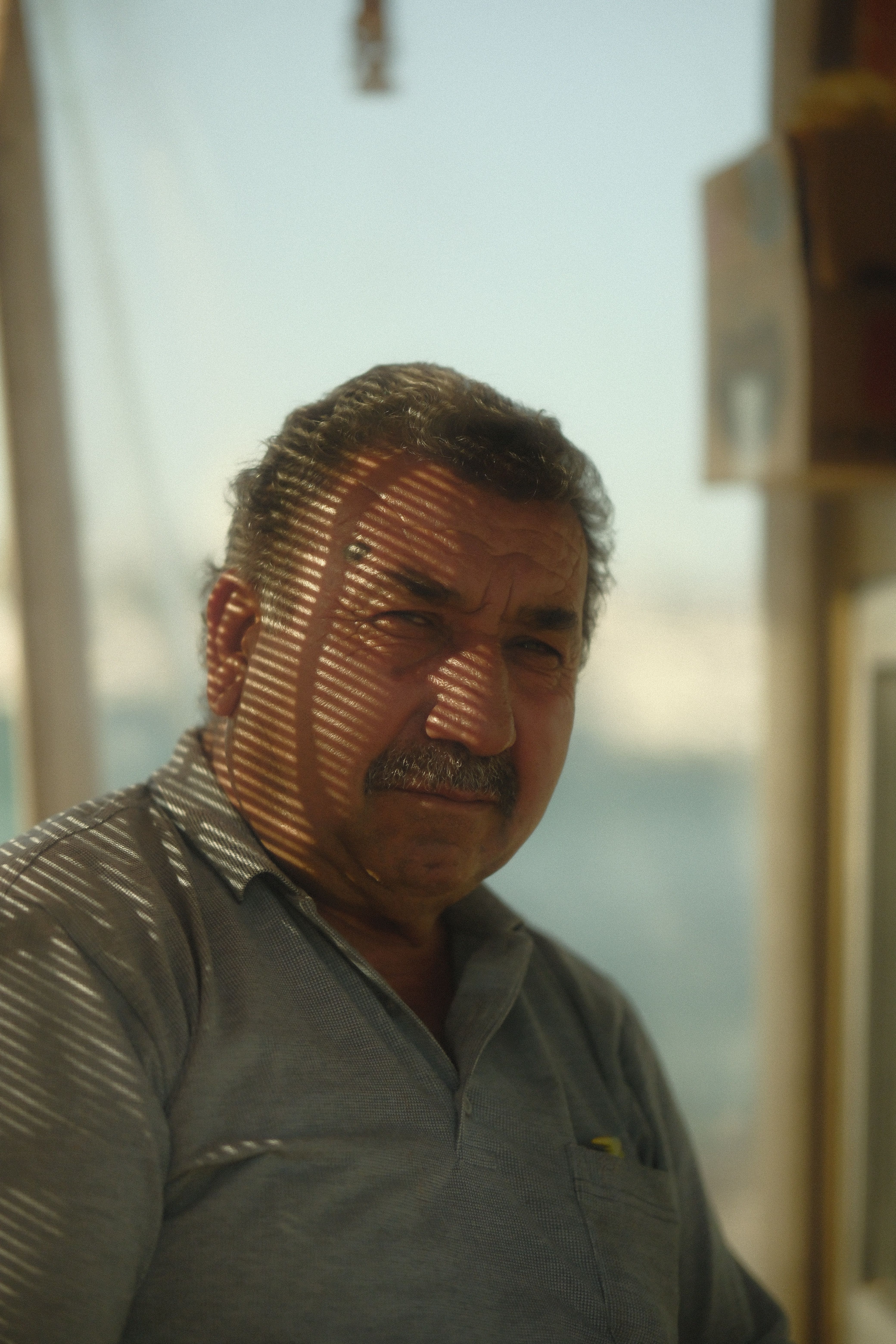Portrait of an elderly man with a mustache in natural daylight, shadows creating intriguing patterns.
