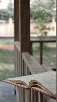 An open book placed on a wooden railing outdoors, inviting relaxation and reflection.