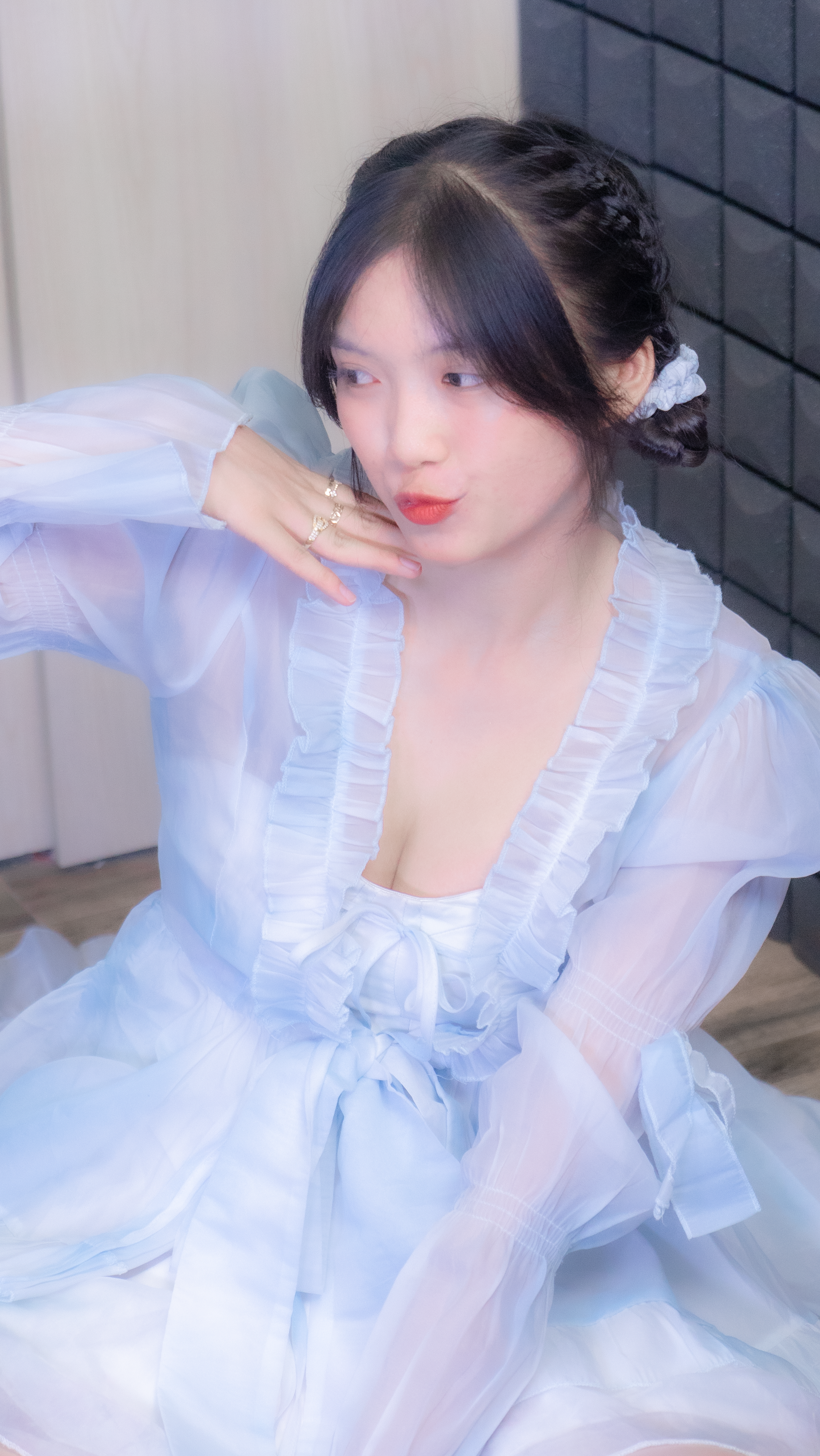 A young woman in a light blue dress poses indoors with a soft, charming expression.