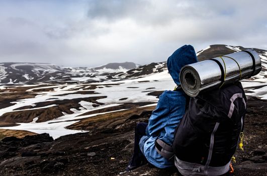A lone traveler rests with a backpack overlooking the snowy terrain of Iceland's mountains.