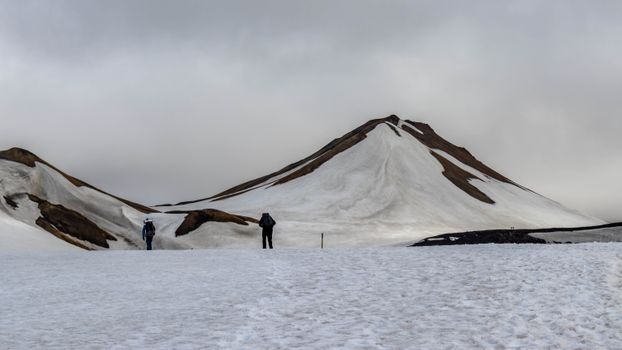 Two hikers trek in the snowy mountains of Iceland, capturing a serene winter landscape.