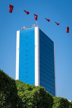 Tall modern skyscraper in Tunis with red flags against a blue sky.