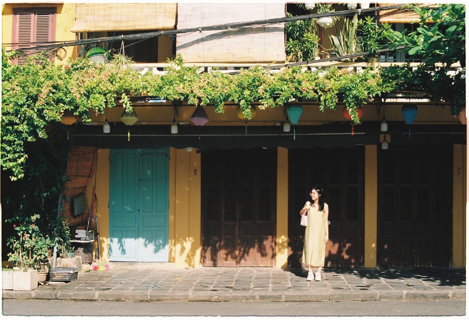 Woman in yellow dress stands in front of a colorful, historic building adorned with greenery.