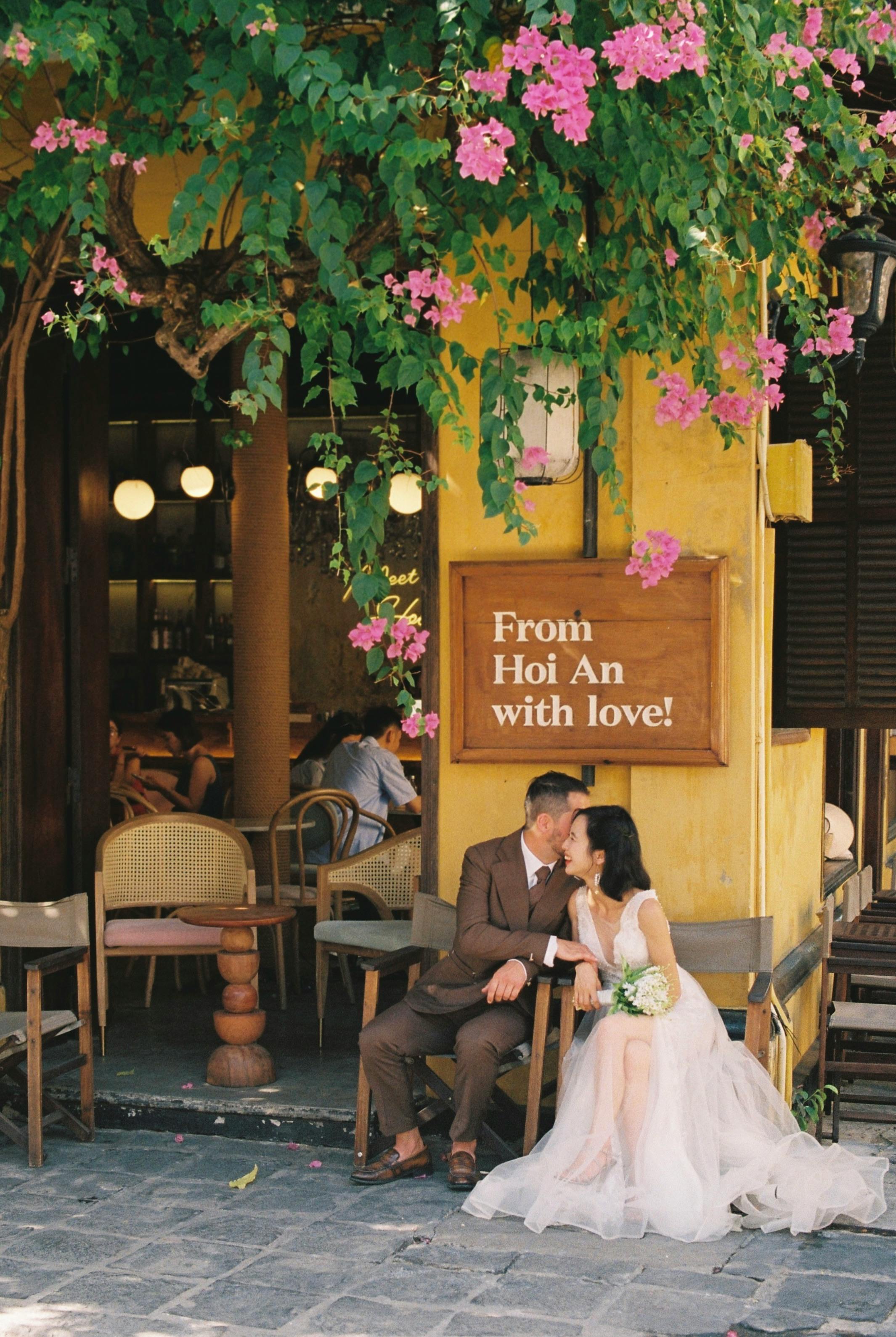 A bride and groom share a romantic moment outside a charming café in Hoi An.