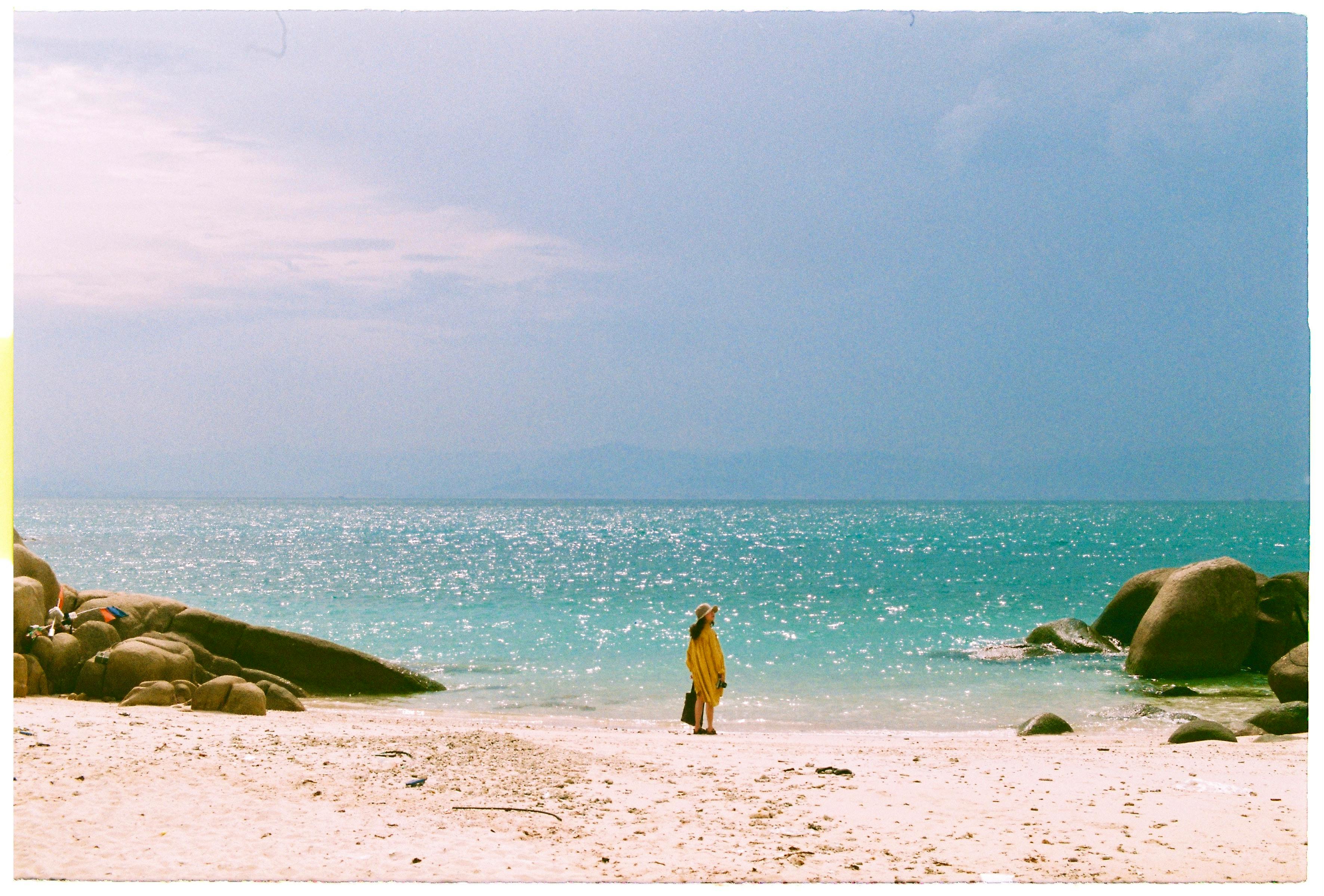 A lone traveler in a yellow dress enjoys a peaceful moment on a tropical beach with turquoise waters.