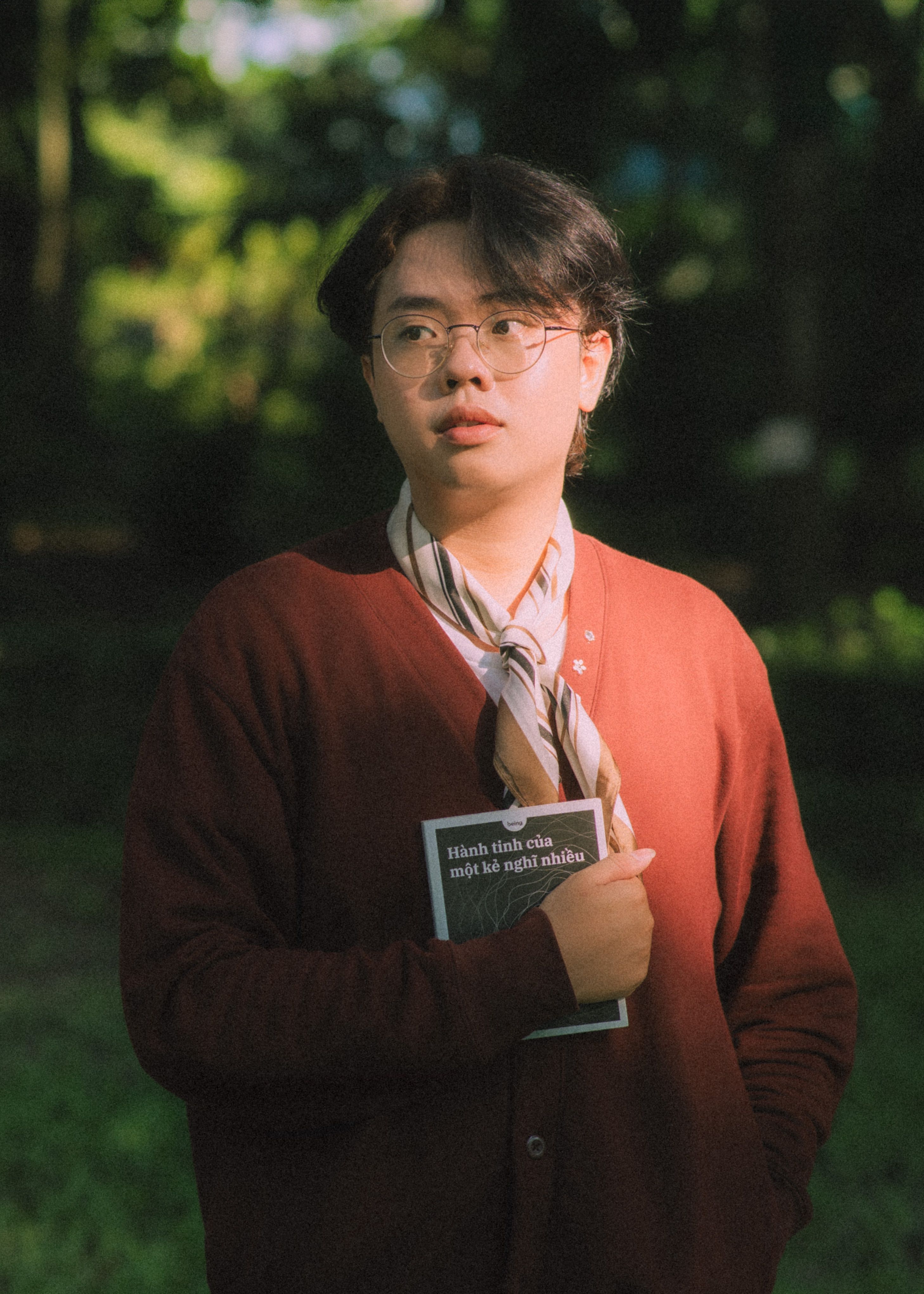 A thoughtful young adult with a book in Hồ Chí Minh, Vietnam, during daylight.