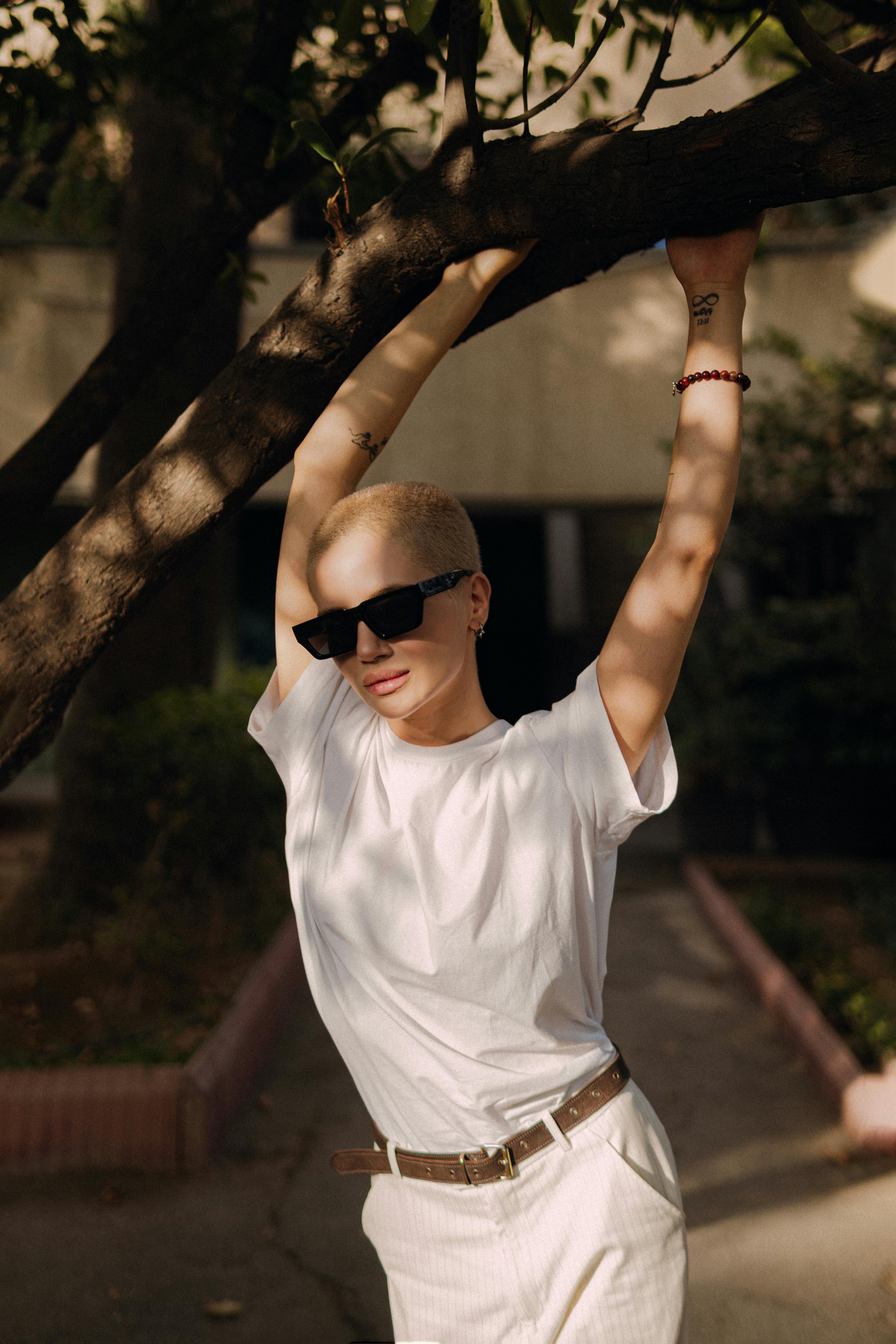 a woman with a shaved head is leaning against a tree